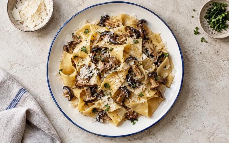 An overhead view of mushroom pappardelle on an ivory plate with a cobalt-blue rim.